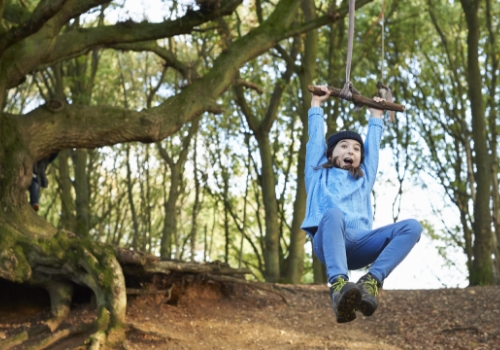 Young girl swinging on a rope swing in woodland