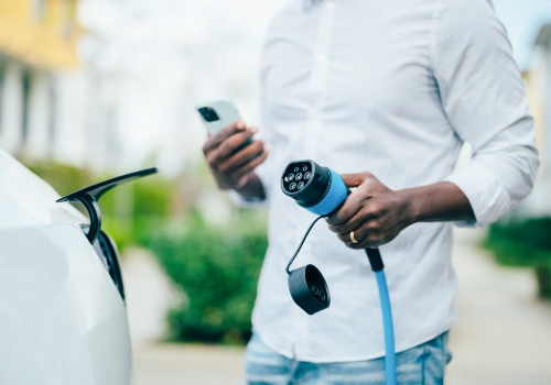 Man charging an electric car with a cell phone in hand  